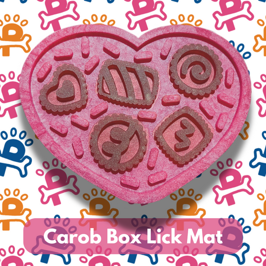 A pink Carob Box Lick Mat designed for dogs, featuring various treat shapes arranged in a heart pattern on a white background with dog graphics.