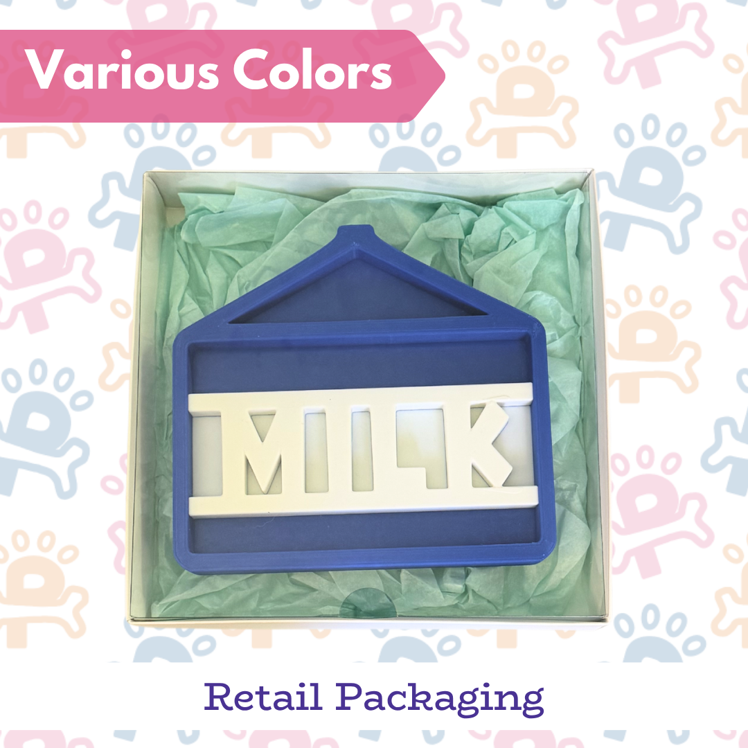 Silicone mold shaped like a house with 'MILK' letters in blue and white, displayed in green packaging with baby-themed background.